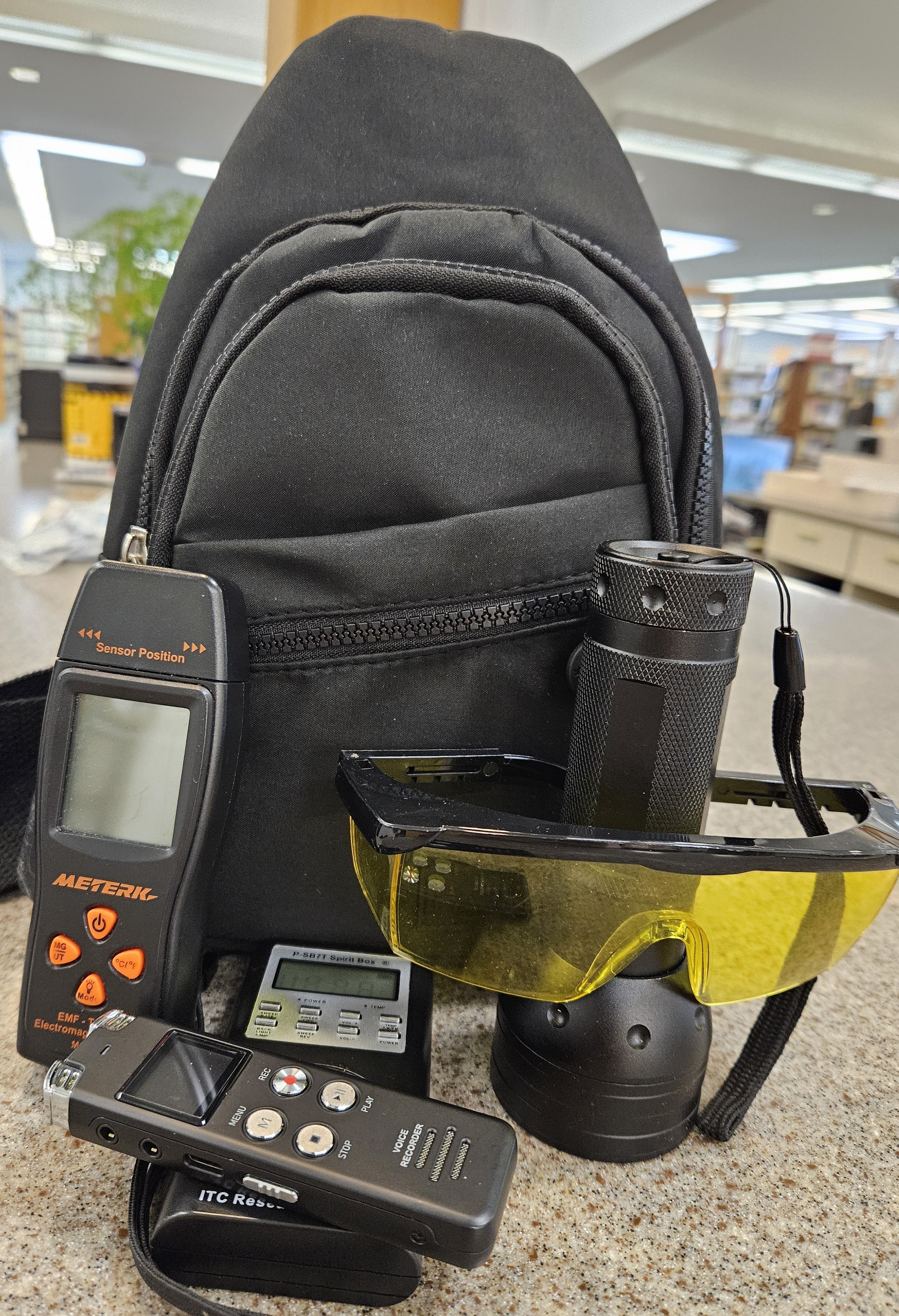Black backpack with various ghost hunting equipment displayed