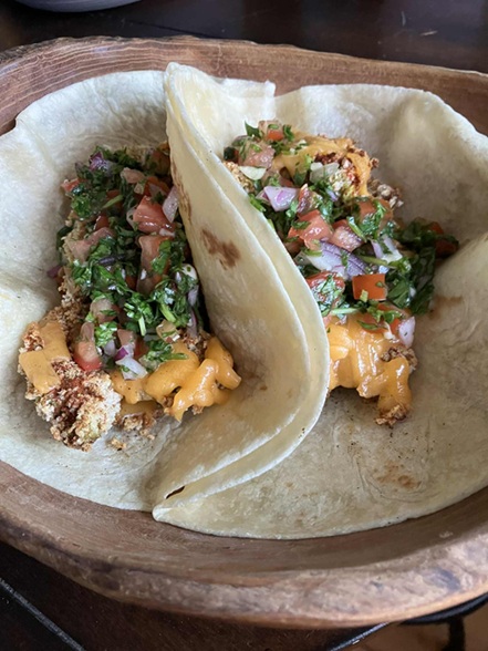 two tacos in flour tortillas with orange sauce, cilantro, onions, tomato