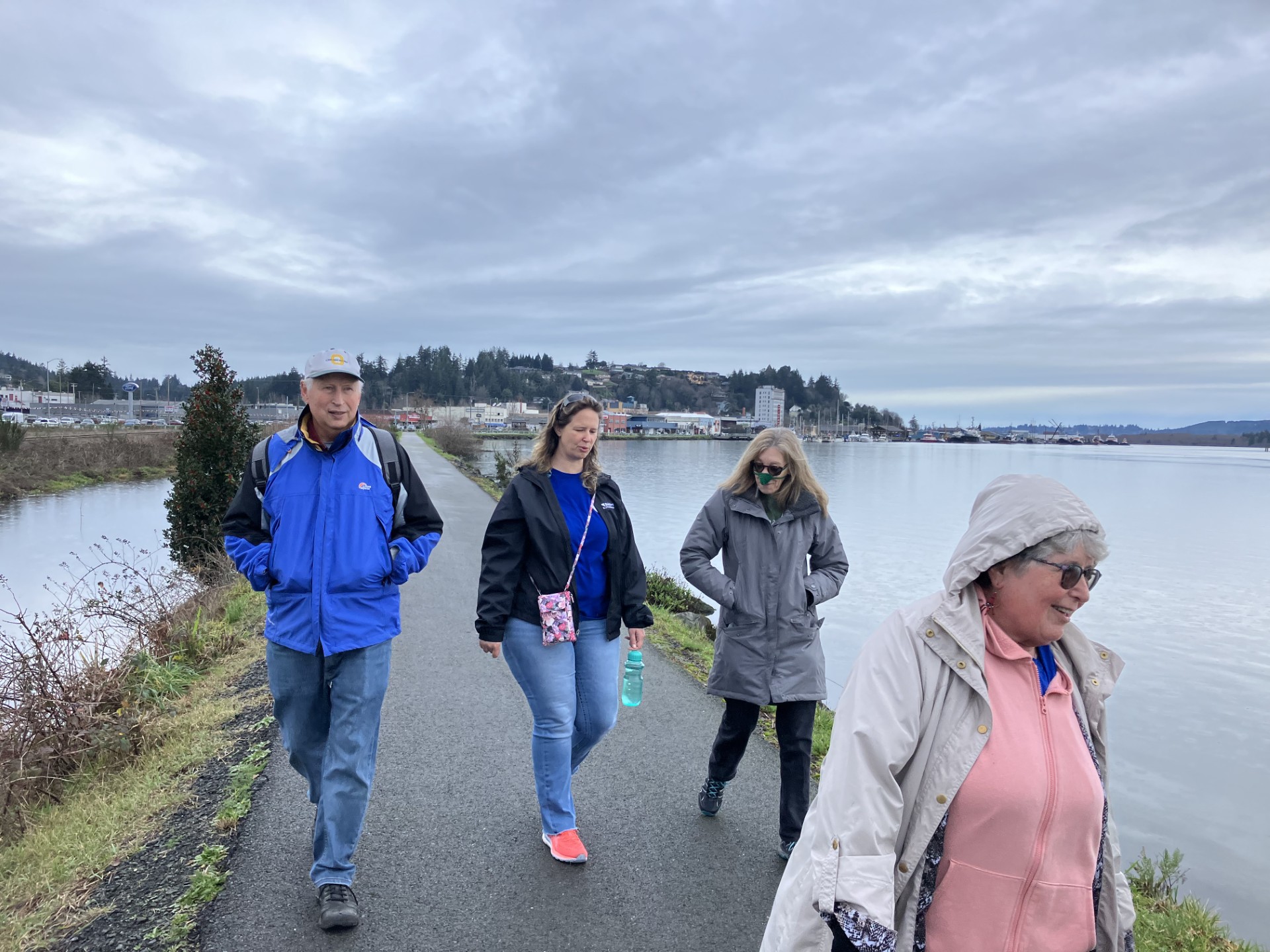 pic of four Sole mates walking Boardwalk trail (view from front), city and cloudy sky behind them