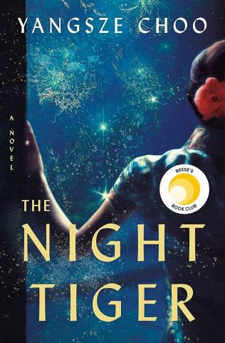 The cover for the book The Night Tiger by Yangsze Choo. The cover is a dark blue sky with a lot of stars. A woman stands  looking out at the stars. 
