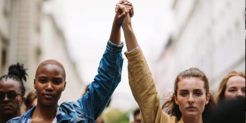 Black woman and white woman, side by side w/clasped hands